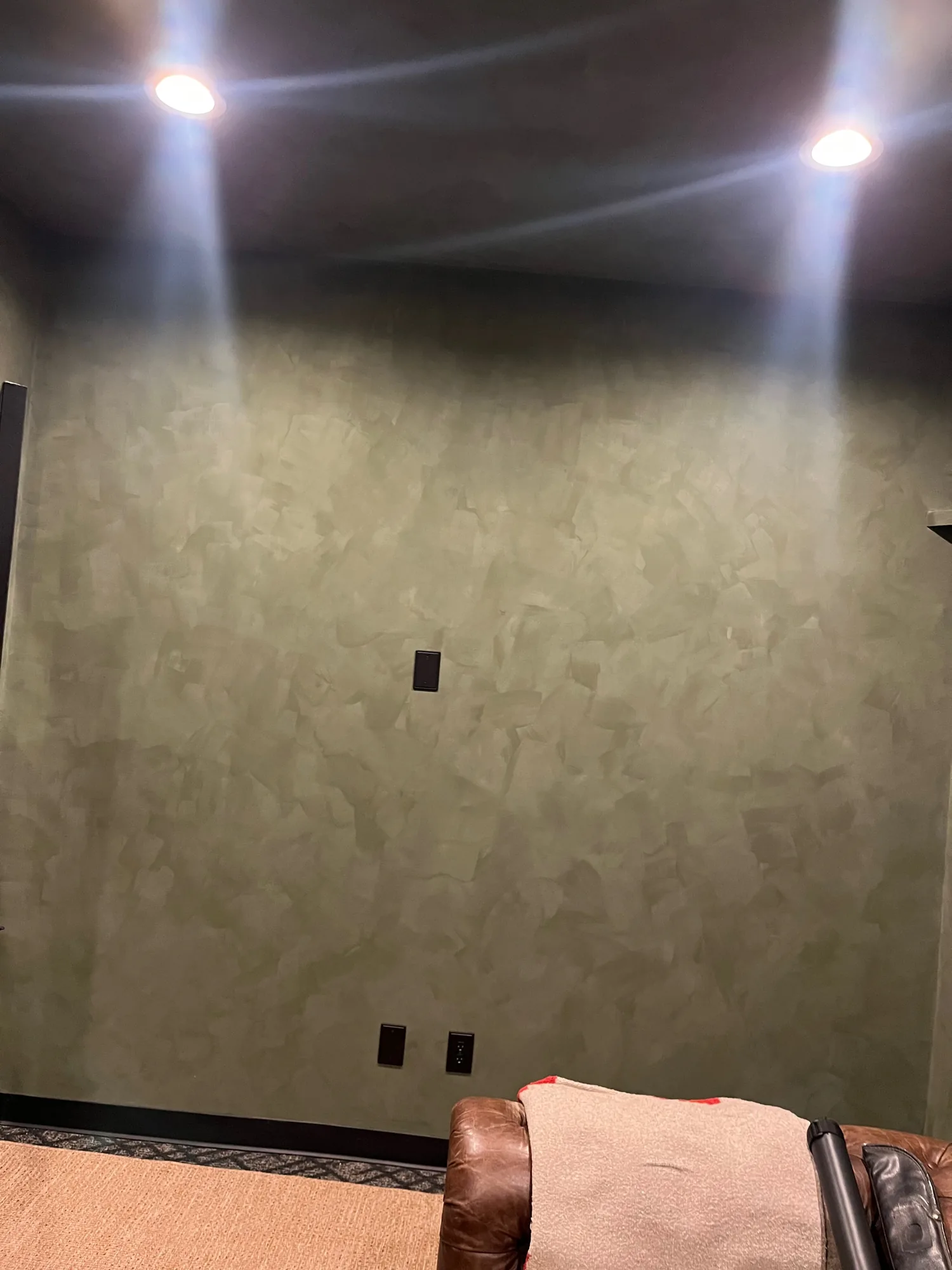 Gray-green textured wall under recessed lights with dark trim and a leather chair at the edge.