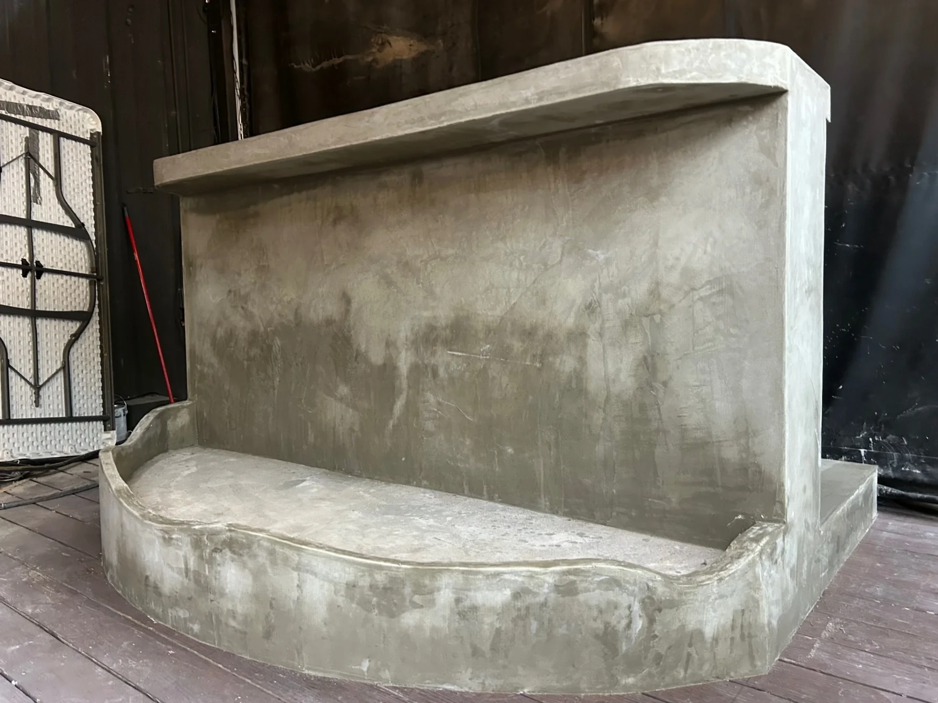 Gray-coated decorative structure with a tall rectangular back, projecting top edge and rounded base on a wood deck.